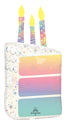 The 28" Holographic SuperShape Pearlized Birthday Foil Balloon by Anagram/MD is shaped like a birthday cake slice with three lit candles, pastel rainbow colors, star and dot patterns, a writable space, and features the Anagram brand logo at the bottom.