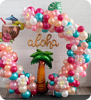 an elaborate circular display featuring balloons in the shape of a palm tree, a tropical drink, leaves, balloons made to look like hibiscus flowers, and many latex balloons in shiny blue, deep red, white, rose, and peach