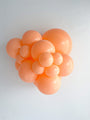 A cluster of TT-260's Designer Cheeky Tuftex Brand Twisting Animal Latex Balloons by Tuftex in various orange sizes is arranged against a white textured wall, resembling a bunch of grapes.