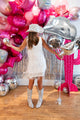 A woman in a white fringe dress, silver glitter boots, and a sparkly cowboy hat smiles in front of pink and silver balloons, holding the Anagram/MD Bouquet Disco Western Foil Balloon.
