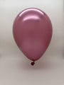 A single 12'' Balloonia Latex Balloon in Brilliant Mauve from the Professional Line is fully inflated and floats against a plain background, with its metallic pink sheen shining. Comes from a 50 per bag pack by the brand Balloonia.