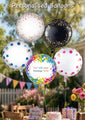 Un globo de papel metalizado confeti rosa dorado de 18" de Oaktree flota al aire libre, rodeado de otros globos de lunares de colores. En la mesa de abajo hay una tarta de cumpleaños, flores y una tarjeta de "Feliz cumpleaños".