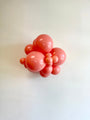 A playful and artistic balloon sculpture is created with a cluster of various-sized Tuftex 17″ Poppy Tuftex Latex Balloons (25 Per Bag), arranged against a plain white wall.