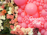 A decorative backdrop featuring 12″ Kalisan Latex Heart Balloons in Queen Pink from Kalisan arranged on the right, accompanied by clusters of colorful artificial flowers on the left.