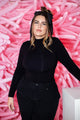 A woman with wavy hair in a topknot and headband wears a black long-sleeve outfit, standing before a backdrop of TT-260’s Baby Pink Tuftex Brand Latex Balloons Twisting Animal Designer Balloons by Tuftex.