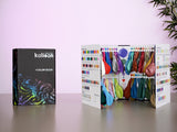 The Kalisan 2026 Latex Balloons Black Color Book Portfolio is open on a table, showing rows of colored balloons and color charts, with the closed portfolio beside it and a plant in the background.